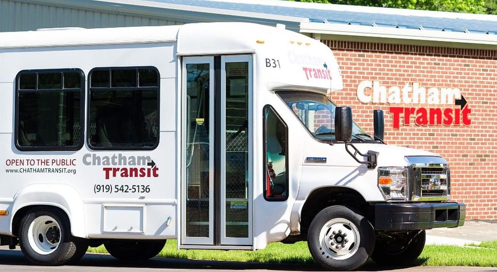 A Chatham Transit bus parked outside the office. The side of the bus reads OPEN TO THE PUBLIC, chathamtransit.org, and (919) 542-5136.